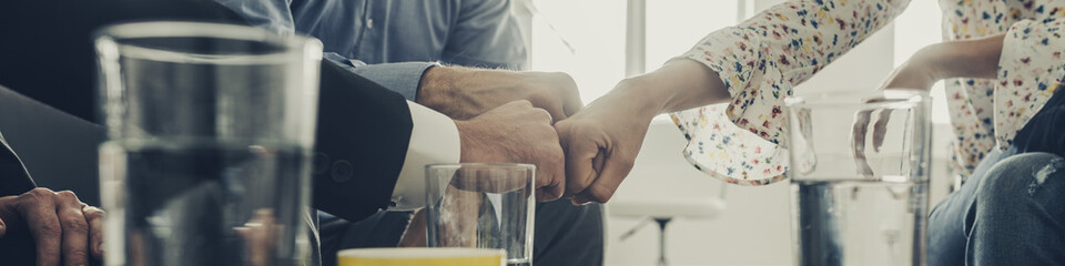 Wide view image of three business people bumping their fists together as they sit in an office meeting.