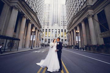 Wall Mural - Elegant bride in a white dress and veil. Handsome groom in a blue suit. Couple in a big city