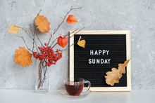 Happy Sunday Text On Black Letter Board And Bouquet Of Branches With Yellow Leaves On Clothespins In Vase And Cup Of Tea On Table Template For Postcard, Greeting Card Concept Hello Autumn Sunday