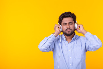 Indian man enjoy the music in his headphones on yellow background with copyspace