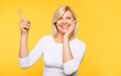 © My Ocean studio - Happy excited beautiful blonde senior woman in casual clothes is pointing away on yellow background.