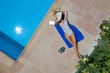Mujer joven en bañador tendida sobre una toalla de manera relajada en una piscina, vista cenital desde el aire