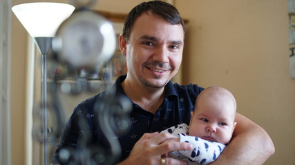 Portrait of loving young man holding baby at home with lamp.