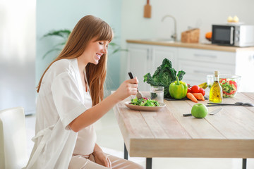 Beautiful pregnant woman eating healthy salad in kitchen