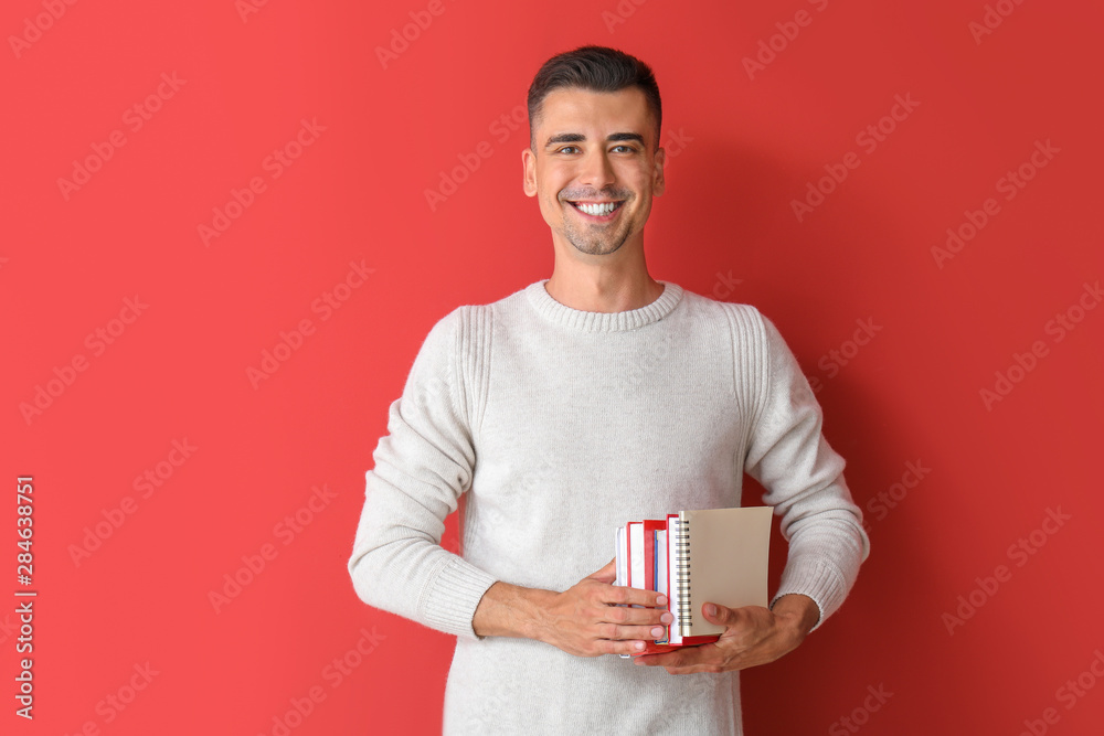 Handsome male teacher with books on color background