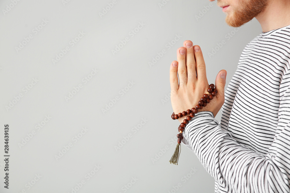 Religious young man praying to God on light background