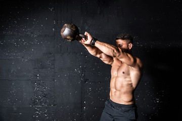 Young strong sweaty focused fit muscular man with big muscles holding heavy kettle bell for swing training hard core workout in the gym 