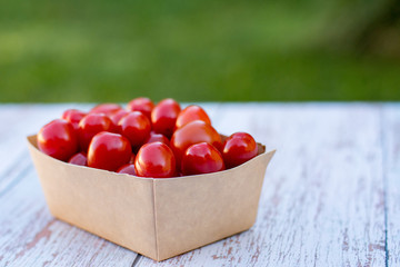 Organic ripe cherry tomatoes in a recyclable paper box on a wooden tablein the garden. Cooking ingredients. Harvest. Sustainable living. Say “no” to plastic packaging.