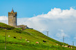 Hill in a field with green grass, cattle grazing with the tower of Doonagore castle in the background, sunny spring day in the coastal town of Doolin in County Clare in Ireland. Wild Atlantic Way