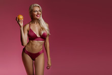 Beautiful Smiling Blonde Woman In A Pink Bathing Suit Smiles And Holds An Orange. Healthy Life. Copy Space