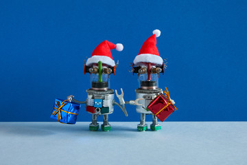 Glass headed Santa Claus robots holds gift boxes. Christmas Happy New Year robotic style greeting poster. Two funny steampunk mechanical toys against blue gray background