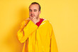 © Krakenimages.com - Young man wearing rain coat standing over isolated yellow background looking confident at the camera with smile with crossed arms and hand raised on chin. Thinking positive.
