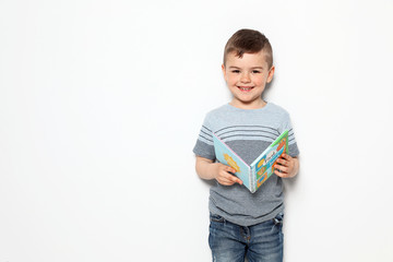 Wall Mural - Cute little boy reading book on white background, space for text