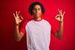 © Krakenimages.com - Afro man with dreadlocks wearing striped t-shirt standing over isolated red background relax and smiling with eyes closed doing meditation gesture with fingers. Yoga concept.