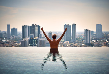 Back view of happy freedom man with raised arms enjoy his summer vacation on swimming pool