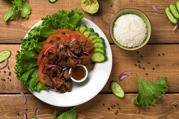  Bo Luc Lac dish on wooden background. Also named Lok Lak in cambodia or Shaking Beef in America. Tasty marinated sauteed beef cubes are served with fresh lettuce, tomatoes, cucumbers, onions and rice