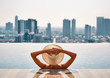 © GVS - Back view of young woman in hat relaxing in swimming pool on the roof top of hotel and enjoy cityscape
