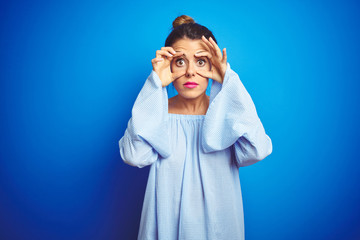 Sticker - young beautiful woman wearing bun hairstyle over blue isolated background trying to open eyes with f