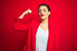 Leinwandbild Motiv Young beautiful business woman standing over red isolated background Strong person showing arm muscle, confident and proud of power