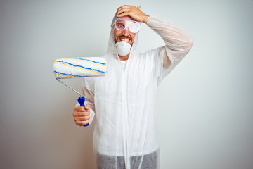 Poster - Painter man wearing professional worker equipment holding roller over isolated background stressed with hand on head, shocked with shame and surprise face, angry and frustrated. Fear and upset 