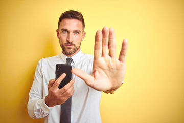 Wall Mural - Young handsome business man using smartphone over yellow isolated background with open hand doing stop sign with serious and confident expression, defense gesture