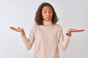 Wall Mural - Young brazilian woman wearing turtleneck sweater standing over isolated white background clueless and confused expression with arms and hands raised. Doubt concept.