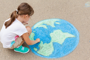 the  child girl draws a planet of the world with colored chalk on the asphalt. Children's drawings, paintings and concepts. Education and art, be creative when you return to school.  earth, Peace day