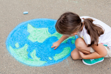 the child girl draws a planet of the world with colored chalk on the asphalt. children's drawings, p