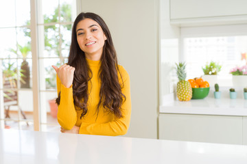 Sticker - Young beautiful woman at home on white table smiling with happy face looking and pointing to the side with thumb up.