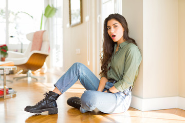 Poster - Young beautiful woman sitting on the floor at home afraid and shocked with surprise expression, fear and excited face.