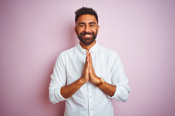 Canvas Print - Young indian businessman wearing elegant shirt standing over isolated pink background praying with hands together asking for forgiveness smiling confident.