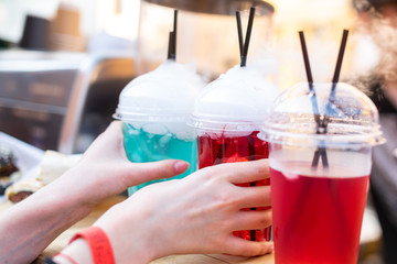 Hands take a multi-colored fruit drink with outgoing steam. Non alcoholic cocktail.