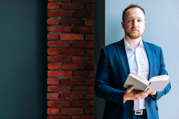 Successful businessman in suit sits holding a book and looks into the camera.