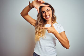 Poster - Young beautiful woman wearing casual white t-shirt over isolated background smiling making frame with hands and fingers with happy face. Creativity and photography concept.