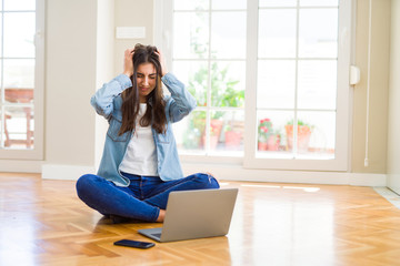 Poster - Beautiful young woman sitting on the floor with crossed legs using laptop suffering from headache desperate and stressed because pain and migraine. Hands on head.