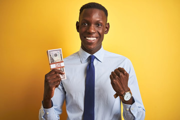 American businessman holding bunch of dollars standing over isolated yellow background screaming proud and celebrating victory and success very excited, cheering emotion