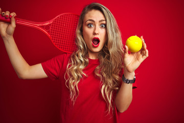 Young sportwoman playing tennis with racket and a ball over red isolated background scared in shock with a surprise face, afraid and excited with fear expression