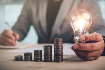 Wall Mural - businessman hand holding lightbulb with coins stacking on desk.saving energy and money concept.