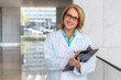 © elnariz - Friendly doctor physician lifestyle portrait, smiling at medical hospital workplace while writing on clipboard