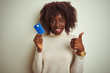 © Krakenimages.com - Young african afro woman holding credit card standing over isolated white background happy with big smile doing ok sign, thumb up with fingers, excellent sign