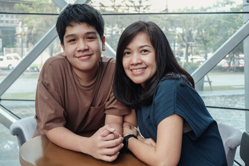 Lifestyle portrait of Asian 40s  mother and teen son spending time together in an urban cafe