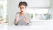 © Krakenimages.com - Beautiful african american woman with afro hair wearing casual striped sweater Moving away hands palms showing refusal and denial with afraid and disgusting expression. Stop and forbidden.