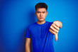 © Krakenimages.com - Young asian chinese man wearing t-shirt standing over isolated blue background looking unhappy and angry showing rejection and negative with thumbs down gesture. Bad expression.