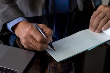 Wall Mural - Business man hand writing and signing checkbook on the wooden table at office. Paycheck or payment by cheque concept.	