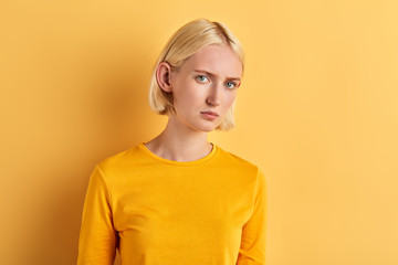 beautiful serious woman with big red ears looking at the camera, isolated yellow background, studio shot. people concept