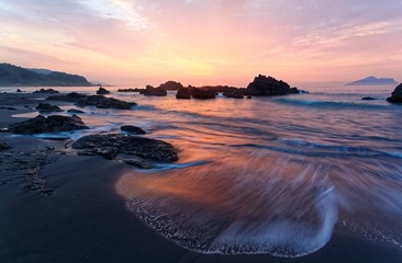 Wall Mural - Sunrise scenery of a beautiful beach on Wai'ao Coast, in Ilan ( Yilan ), Taiwan with golden sunlight reflecting on the water & sea waves rushing upon the shore in rosy twilight (Long Exposure Effect)