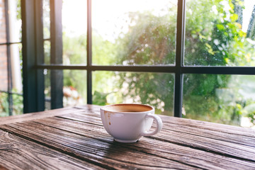 A white mug of hot coffee on wooden table in the morning