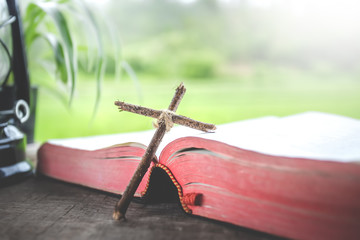 Poster - wooden cross standing with bible on wooden table with green background in morning.