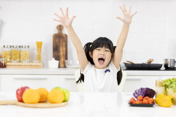 Portrait of Asian little girl Smiling at you in the kitchen and salad ingredients on table at home. Healthy food concept