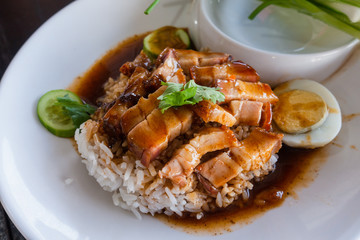 Close up rice crispy pork, roasted red pork, Scallion and boiled egg with sauce in white plate on wooden table background.